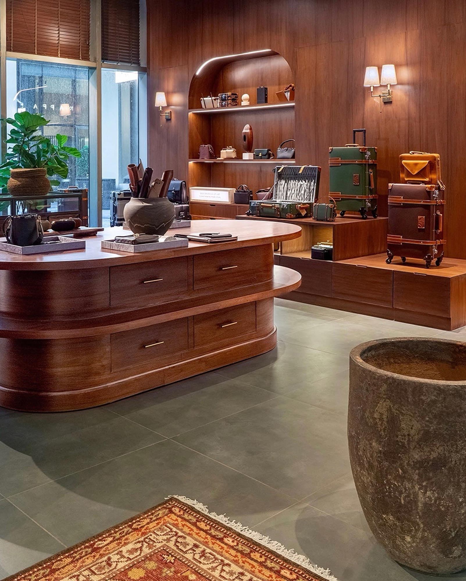 Boutique interior with a curved walnut counter, display niches, luggage and a large stone urn